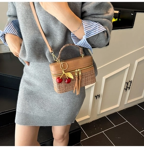 Brown box-shaped bag with woven texture, leather trim and a cherry charm detail