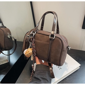Detailed shot of brown suede Boston bag with shiny leather handles and a baseball charm