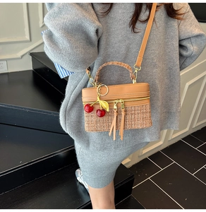 Detail of brown patchwork handbag featuring plaid texture and cherry charm accessory