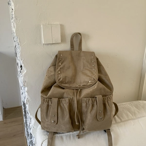 Close-up of camel suede backpack featuring round metal rivets and drawstring closure details