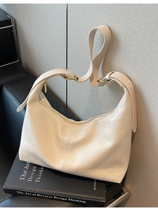 Creamy white vintage leather crossbody bag with adjustable gold hardware on black sofa