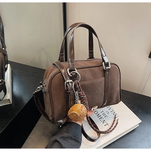 Detail of brown suede boston bag with glossy leather handles and a baseball glove charm