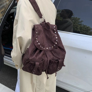 Detail of burgundy suede backpack with silver studs and buckle pockets on a beige coat