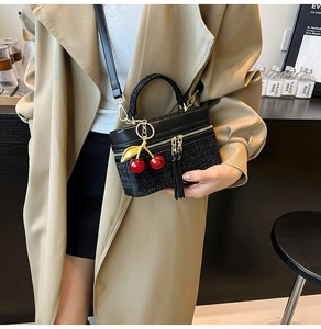 Fashionable tweed and leather handbag detail showing red cherry charm and braided handle