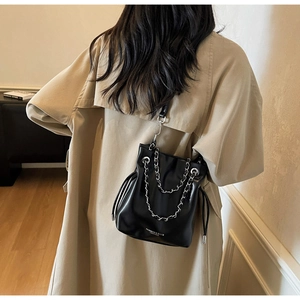Detail of black drawstring bucket bag with silver chain worn over a khaki trench coat