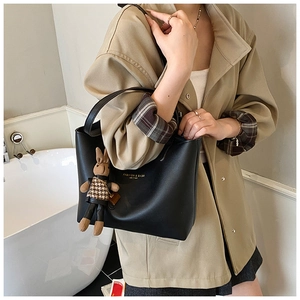 Détail d'un sac cabas en cuir noir avec lettrage doré et un pendentif lapin à carreaux