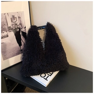 Close-up of black fuzzy plush tote bag with leather handle on an artistic desk setup