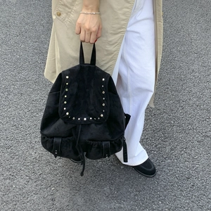 Detailed close-up of a black suede backpack with silver rivets and buckle front pockets