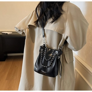 Detail of a black leather bucket bag with silver chains worn with a beige trench coat