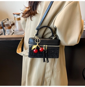 Detail of black tweed and leather crossbody bag with a decorative red cherry charm