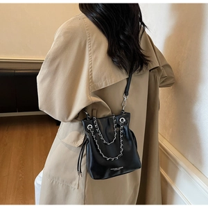 Detail of black leather bucket bag with silver chain worn by a model in a trench coat