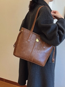 Brown vintage large capacity tote bag with gold metal hardware on grey coat