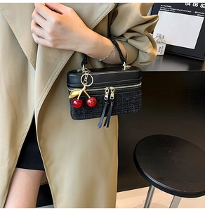Detail of black tweed patchwork handbag with cherry charm and leather tassel zipper