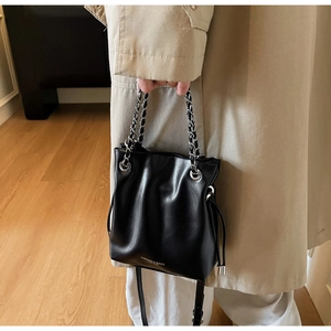 Detail of black drawstring bucket bag with gold lettering and woven chain handle