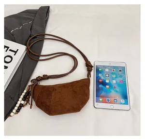 Detailed close-up of brown suede croissant bag showing beaded charm and strap knot detail