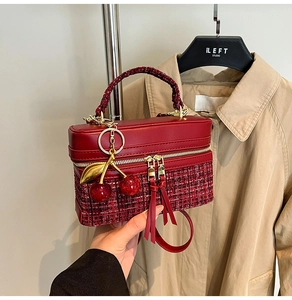 Detail view of red tweed and leather handbag with a decorative cherry charm