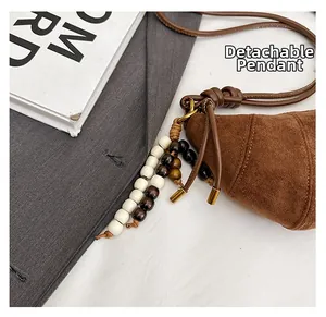 Detail view of a suede crescent bag with a detachable wooden and white beaded charm