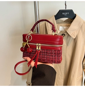 Detail of red tweed and leather handbag with gold zippers and cherry charm accessory