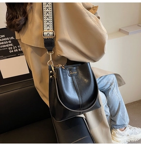 Detail of black faux leather bucket bag with jacquard strap and gold logo lettering