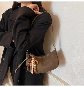 Close-up of brown suede crescent bag with decorative colorful wooden bead tassel details