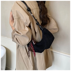 Détail d'un sac demi-lune en daim noir avec noeud de bandoulière et charm chocolat