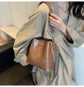 Detail of vintage brown bucket bag with wide woven strap and polished PU leather texture