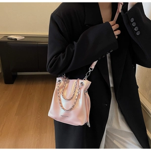 Pink glossy bucket bag with silver chain handle worn over a black blazer suit