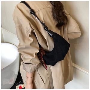 Vue détaillée du sac croissant en daim noir avec ruban porté sur un trench-coat beige