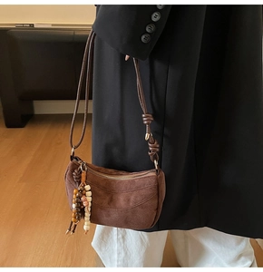 Dettaglio borsa a spalla in camoscio marrone con nappa di legno e tracolla annodata