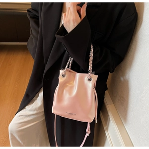 Detail of pink pearlescent leather bucket bag with chain handle on a black blazer