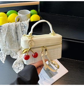 Detail of cream white quilted handbag featuring gold zippers and a red cherry pendant