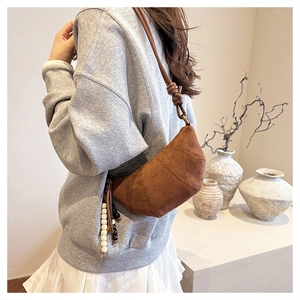 Detail of a brown suede croissant bag featuring unique knot strap and round wooden beads