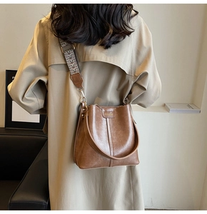 Brown leather bucket bag detail with vintage stitching and patterned woven wide strap