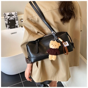 Detail of black faux leather pillow bag with silver zipper and brown bear keychain charm