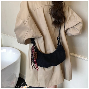 Détail d'un sac hobo en daim noir avec breloque chocolat et gland tressé