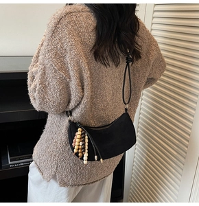 Dettaglio borsa a mezzaluna nera opaca con nappina di perline boho su maglione caldo