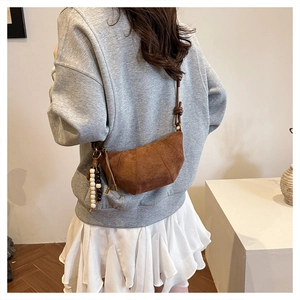 Brown suede crescent bag detail featuring vertical quilting and a beaded tassel charm