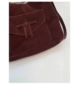 Detailed close-up of premium burgundy suede shoulder bag with signature T-shaped flap closure