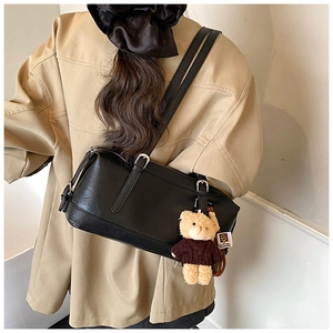 Detail of black leather shoulder bag featuring a cute teddy bear plush charm and silver buckle