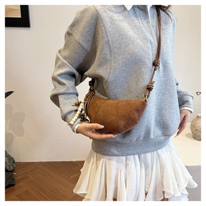 Detail of a brown suede half-moon bag with knot strap and white bead pendant charm
