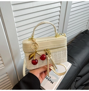 Detail of cream PU leather and tweed crossbody bag with golden zippers and cherry charm