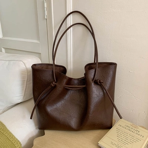 Detail of dark brown leather tote bag with elegant knot drawstrings on a wood surface