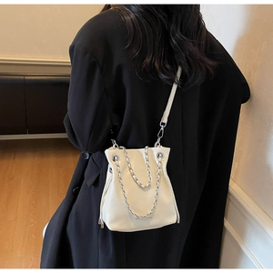 White bucket bag with silver chain detail worn by model over a black winter coat