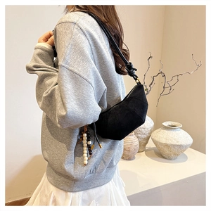 Detail of black crescent shoulder bag with wooden bead tassel and geometric stitching