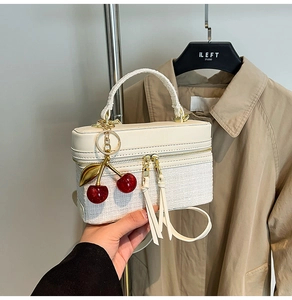 Detail of cream vanity bag featuring tweed texture and red cherry metallic pendant