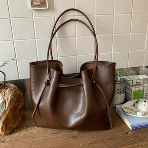 Detailed view of dark brown tote bag featuring drawstring pleats and leather texture