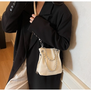 Detail of a creamy white bucket bag with silver chain and metal clasp on a model