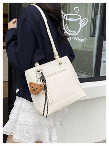 Detail of off-white lychee grain tote bag with plush bear charm in outdoor street setting