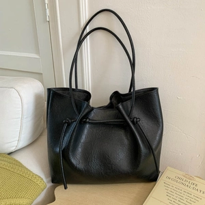 Detail of black tote bag with lychee texture, drawstring knot, and long thin shoulder straps