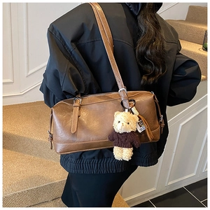 Close-up of retro brown leather Boston bag with cute teddy bear pendant on shoulder strap